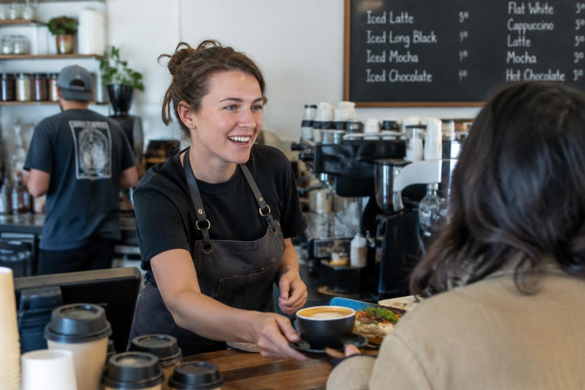 A casual worker serving customers at a busy cafe counter